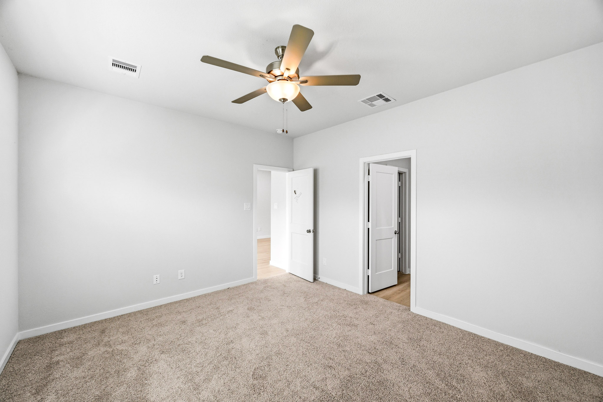 A room with a ceiling fan and a carpet.