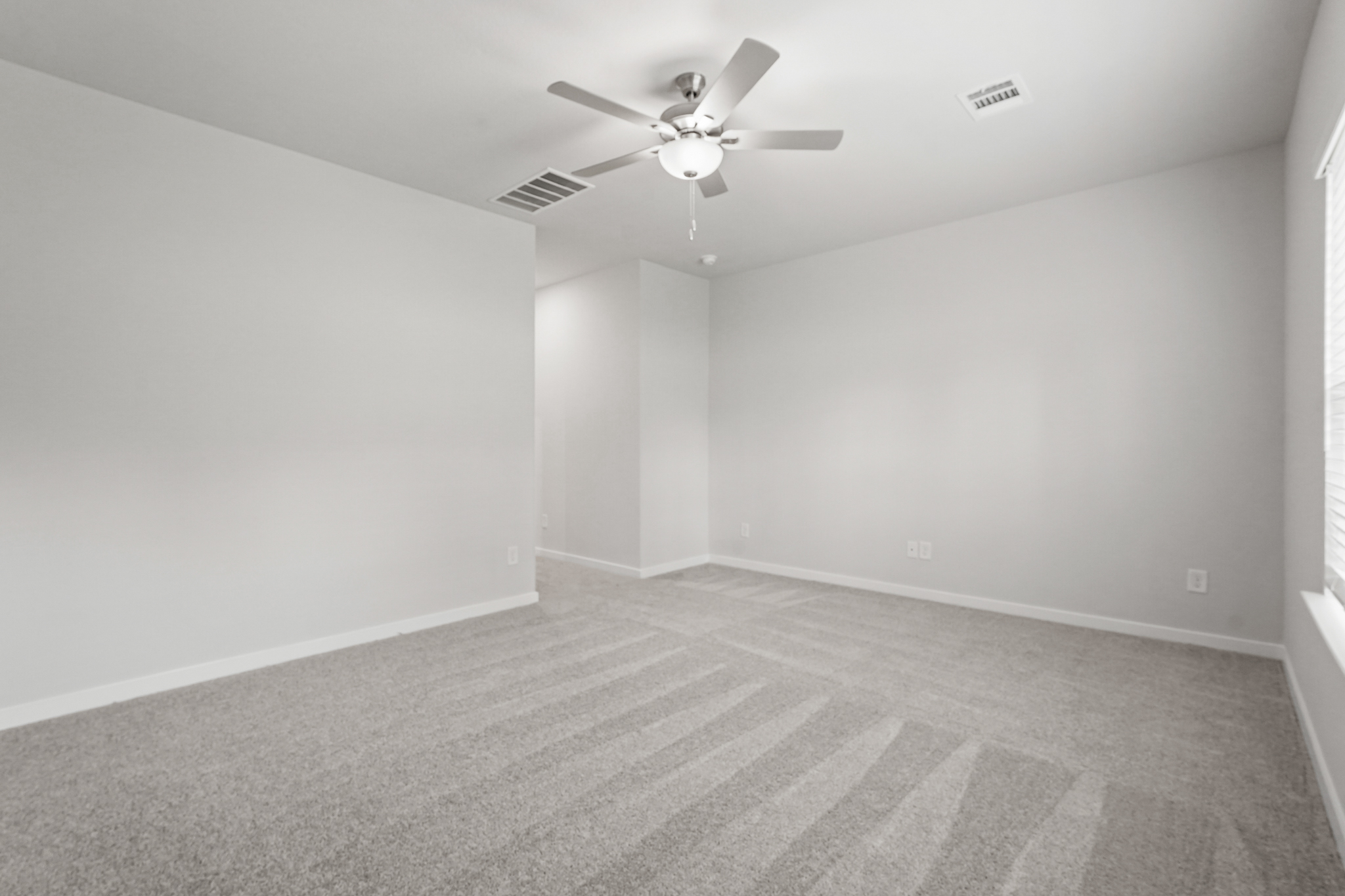 A room with a ceiling fan and a carpet.