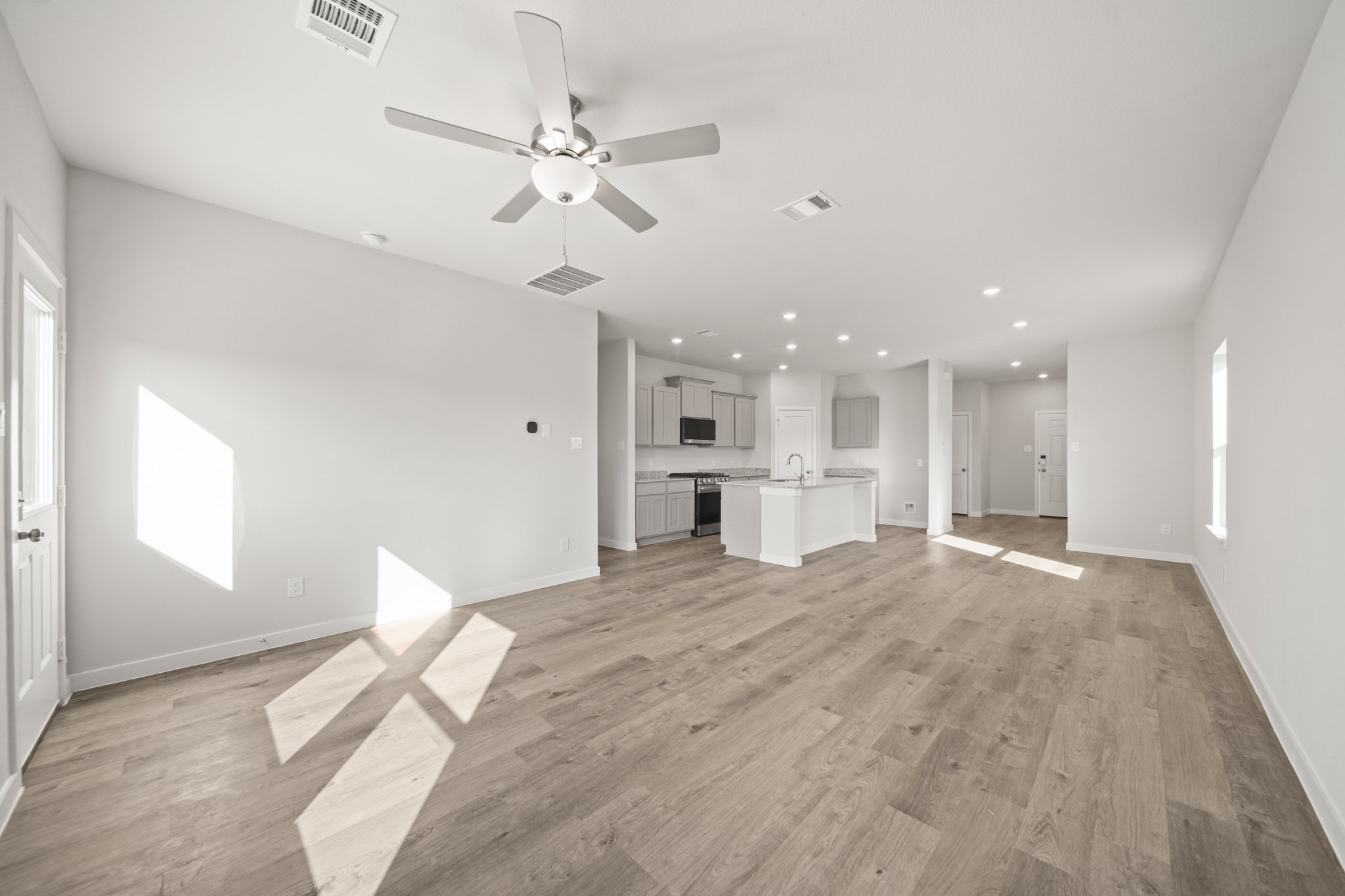 A large empty room with a ceiling fan and a wood floor.